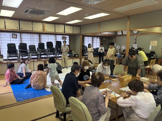 住民が畿央大学生と一緒に大きな佐味田地区の地図に絵を描いたり板絵やキューブを作成している様子